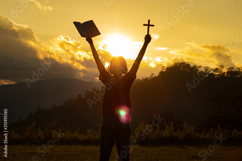 Silhouette of woman praying with cross in nature sunrise background, Crucifix, Symbol of Faith. Christian life crisis prayer to god.