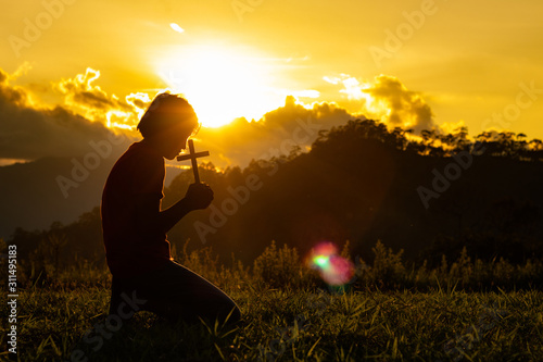 Silhouette of woman praying with cross in nature sunrise background, Crucifix, Symbol of Faith. Christian life crisis prayer to god.