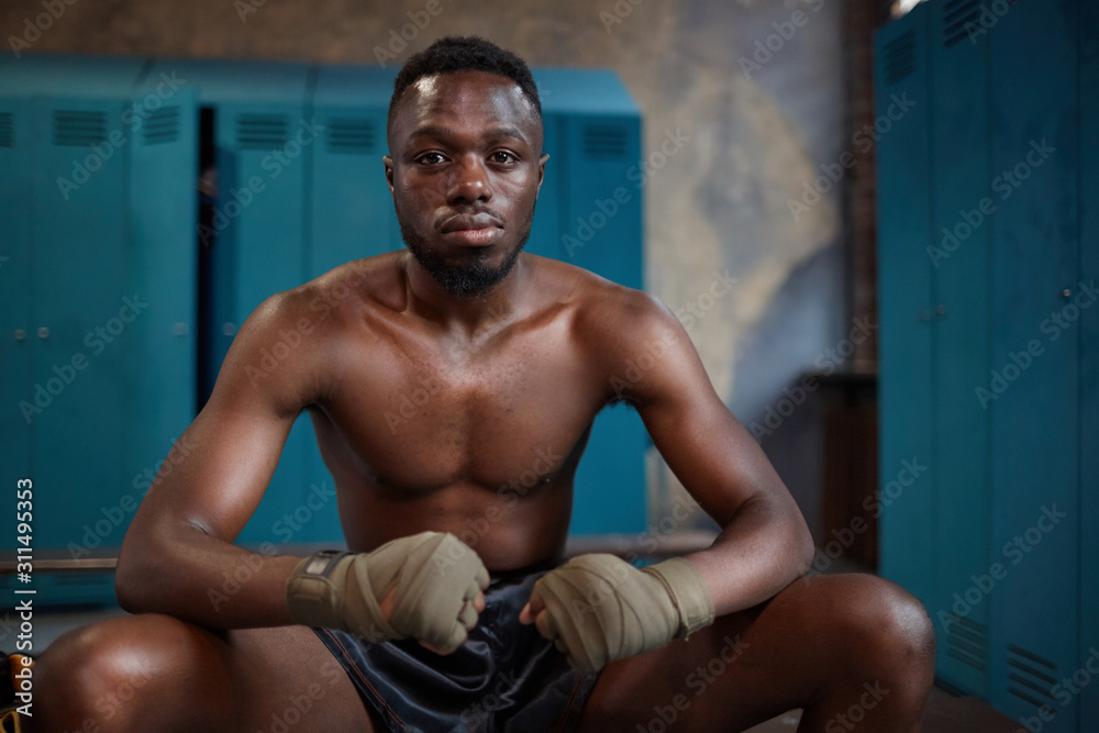 Portrait of African young boxer looking at camera while sitting on bench in locker room Portrait of African young boxer looking at camera while sitting on bench in locker room