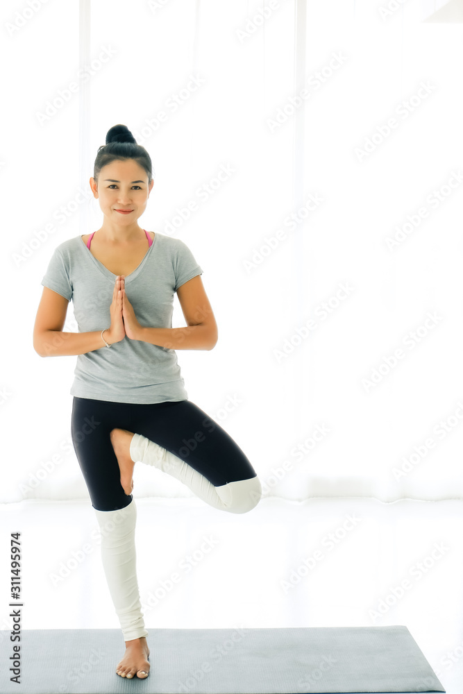 Asian smile woman practicing yoga at home, standing in Vrksasana or Tree pose,working out, wearing sportswear, concept of healthy life and natural balance
