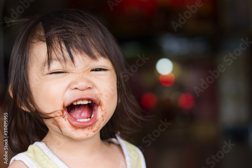Portrait image of 1-2 yeas old baby. Happy Asian child girl eating a brown chocolate by herself. Her face messy and dirty by food.