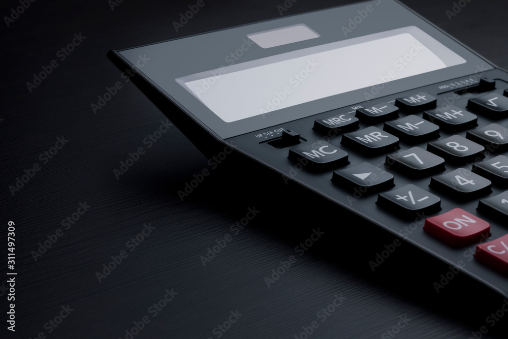 Closeup side view on a big black accounting calculator with blank screen and copy space. Profit and market analysis, calculation of taxes and expenses, saving money and family budget concept Closeup side view on a big black accounting calculator with blank screen and copy space. Profit and market analysis, calculation of taxes and expenses, saving money and family budget concept