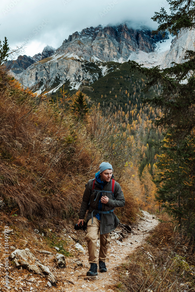 Obraz premium Young male dressed in colourful jacket standing on the ''lago di sorapis'' trail in Italian alps / Dolomite mountains in background during sunset / High ISO image