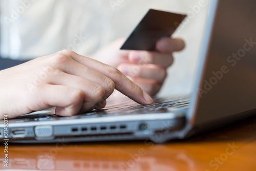 Features holding a credit card and using a laptop for online shopping.