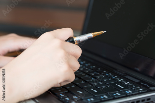 A businesswoman with a pen is using a laptop in her office.