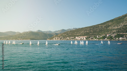 Row of training sailboats on a tugboat is passing by the hilly seashore