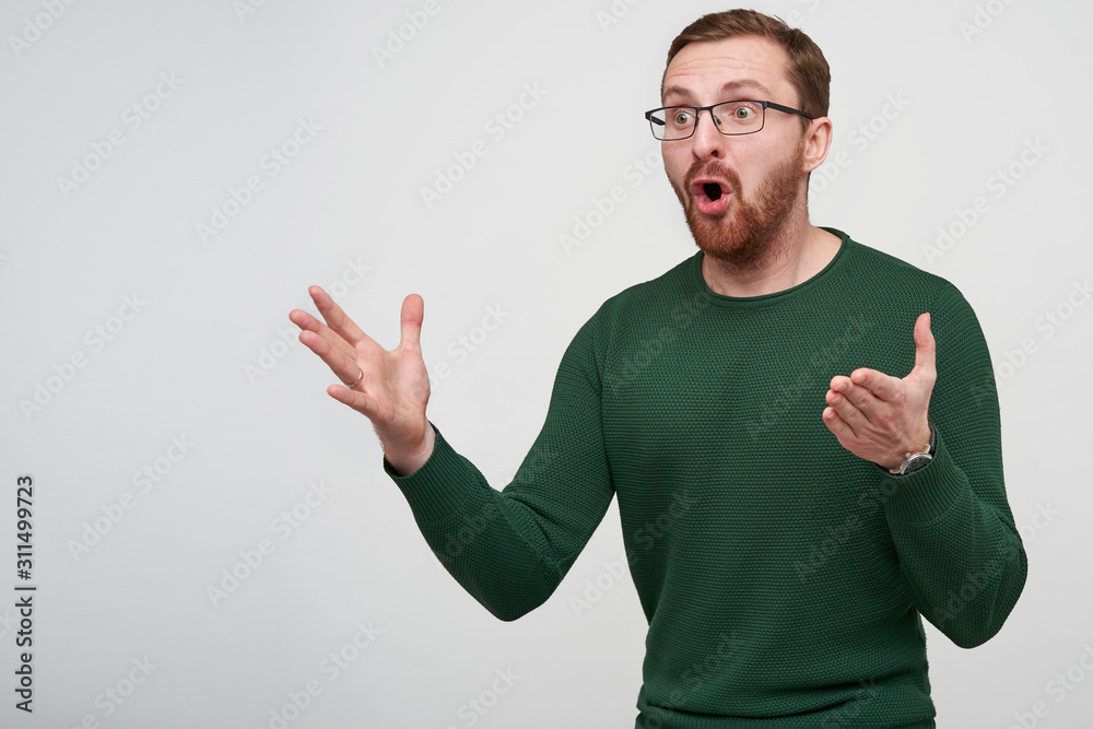 Portrait of young energized brown haired bearded guy in eyewear looking aside with wide eyes and mouth opened and raising emotionally his hands, isolated over white background Portrait of young energized brown haired bearded guy in eyewear looking aside with wide eyes and mouth opened and raising emotionally his hands, isolated over white background