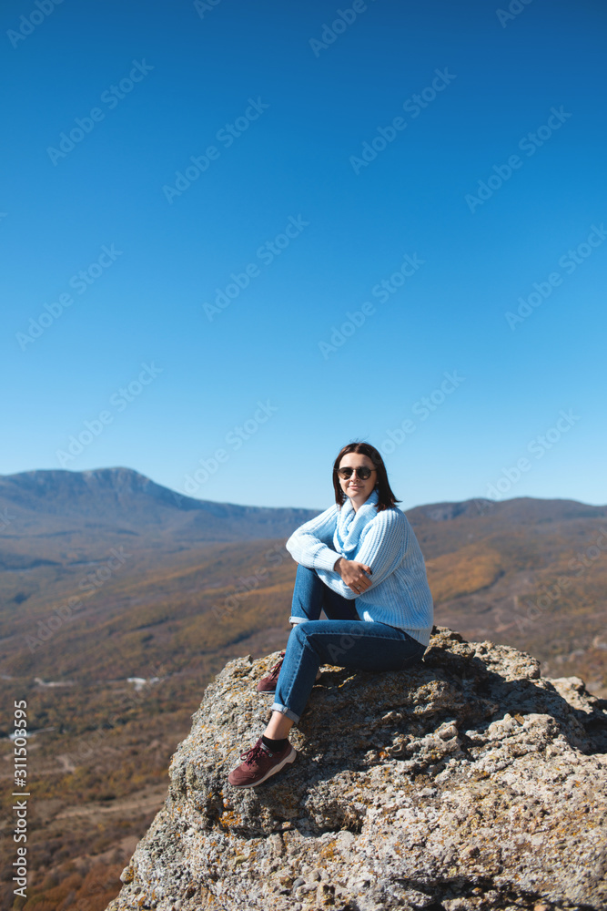 A girl sits on a rock in the mountains and enjoying view of nature. Nature background. Journey. A trip to the mountains.