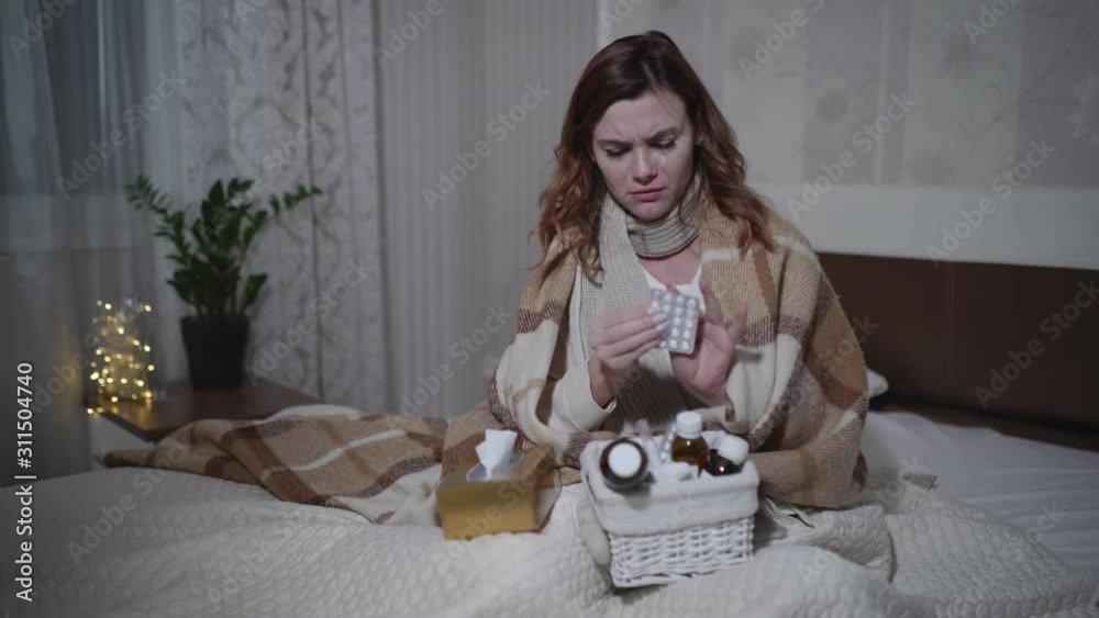 sick girl with a temperature takes pills while sitting on a sofa with a warm blanket, young woman feels bad during the flu or fever at home sick girl with a temperature takes pills while sitting on a sofa with a warm blanket, young woman feels bad during the flu or fever at home