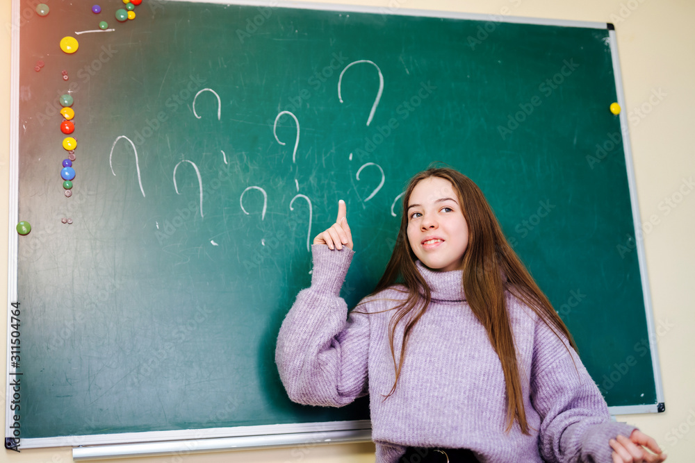 Question mark written on blackboard, cute girl pointing on. School education concept.