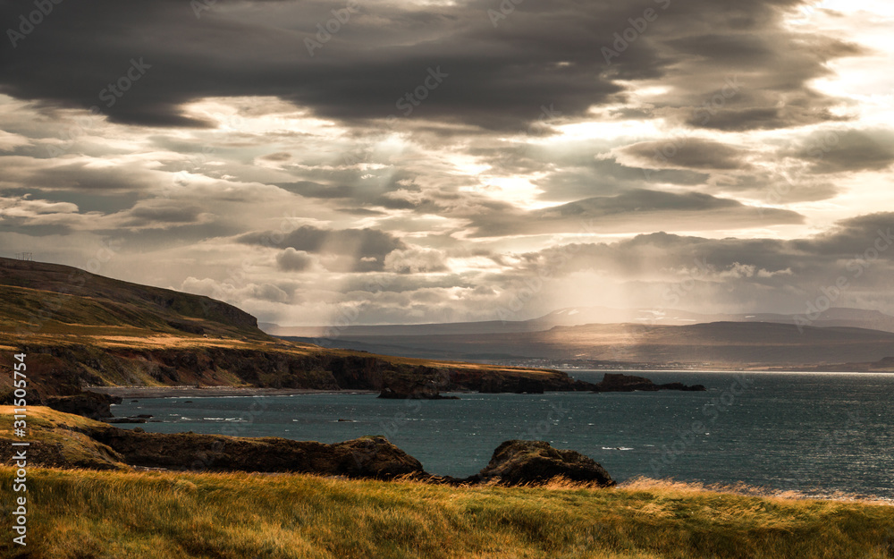 Stormy sky with nice light beams over grassy fields at Icelandic coast