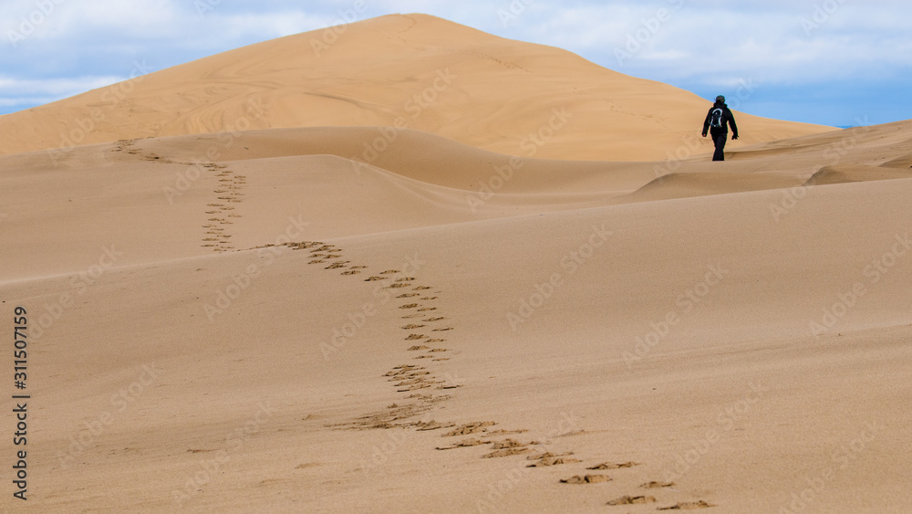 Fußspuren auf Sanddüne mit weglaufender Person im Hintergrund