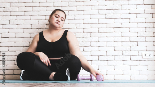 Asian chubby woman sitting on a yoga mat and feeling unhappy to exercise.