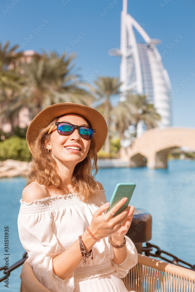 Happy girl using social media and Internet surfing with a smartphone on the background of a skyscraper in Dubai, UAE
