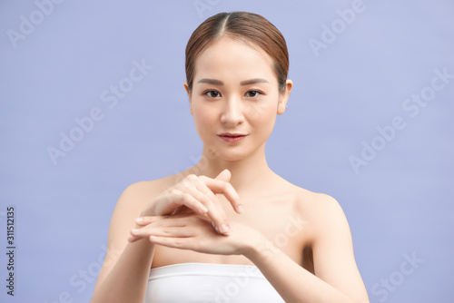 Attractive young woman applying hand cream on violet