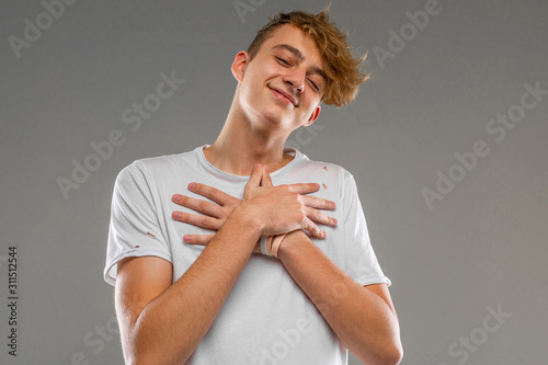 caucasian blond guy in a white T-shirt crossed his arms over his chest on a gray background