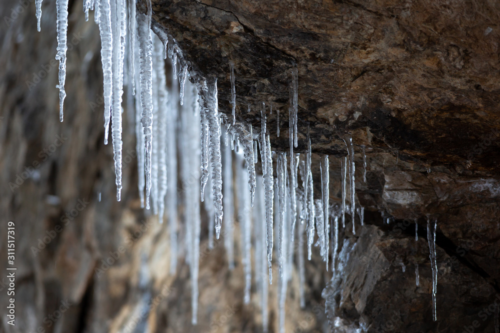 Icicles hang from a cliff. Long transparent and beautiful icicles on stones. Icicles hang from a cliff. Long transparent and beautiful icicles on stones.
