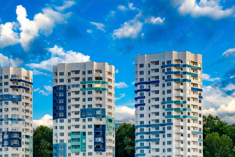 Three tall apartment buildings against a bright blue sky