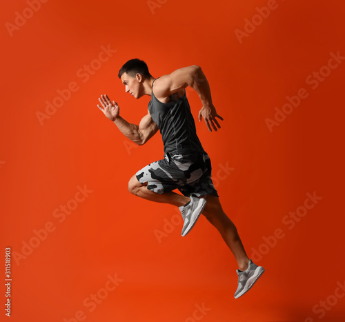 Fototapeta Naklejka Na Ścianę i Meble -  Athletic young man running on red background, side view