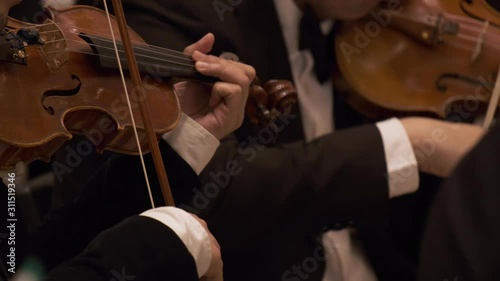 Symphony orchestra on stage, hands playing violin. Shallow depth of field