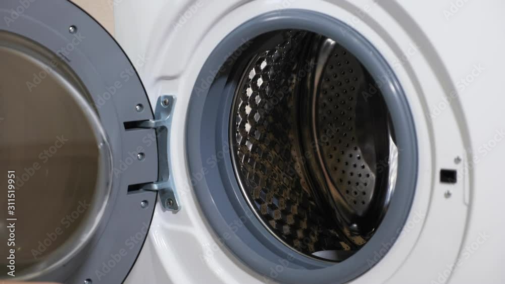 pretty housewife loads dirty clothes into new washing machine sitting on wooden floor in light room closeup pretty housewife loads dirty clothes into new washing machine sitting on wooden floor in light room closeup