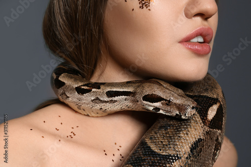 Young woman with boa constrictor on grey background, closeup