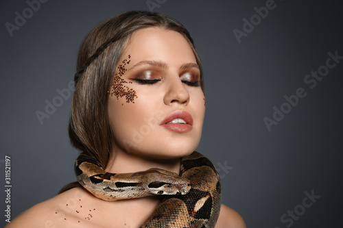 Beautiful woman with boa constrictor on grey background