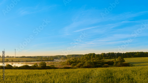 dawn with a view of the field and the river with three cell towers on the shore with clouds in the sky. © StockAleksey