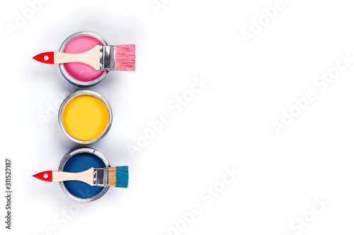 Renovation picture. Isolated white background with three pink, yellow and classic blue pain cans and two brushes. Flat lay, top view, copy space.