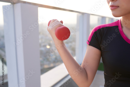 Beautiful young Asian woman practicing with dumbbells outdoor. Sporty girl.
