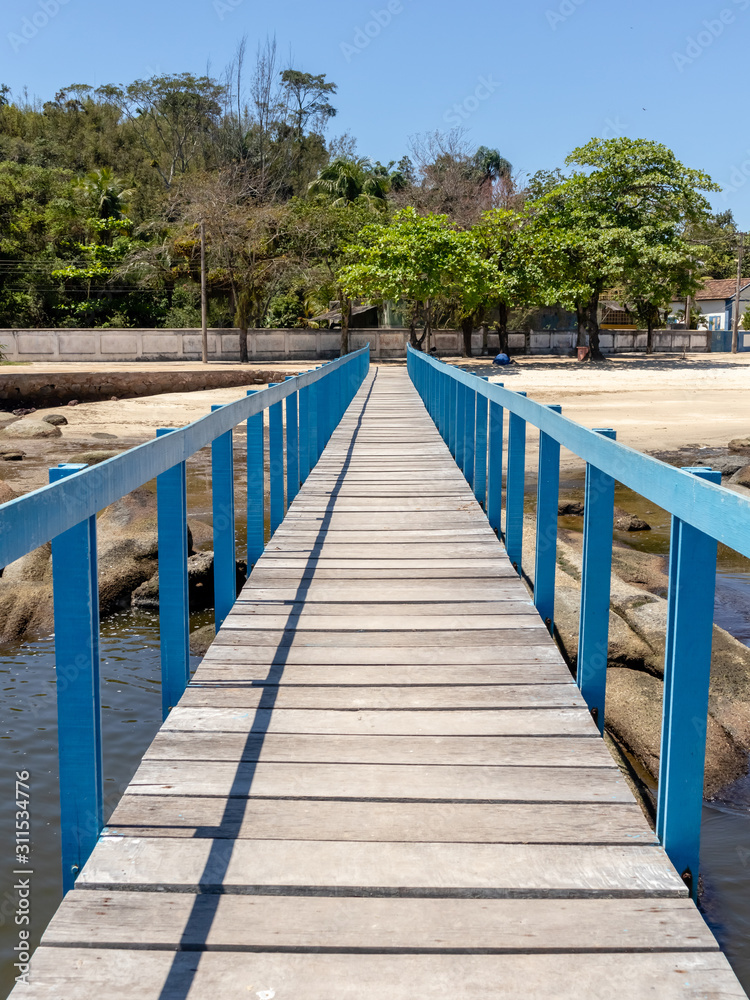 Long wooden pier over rocks on the way to the coast with trees in the background, Paqueta Island, Rio de Janeiro, Brazil