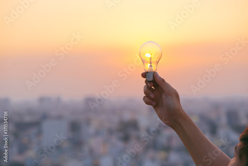 Hand hold a light bulb on sunset background for saving energy and creative concept. photo