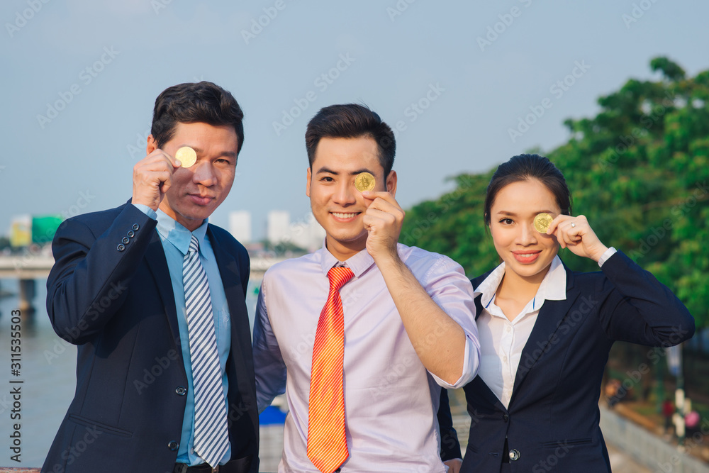 Young Asian Businessman holding golden bitcoin in front of his international Multi ethnic team in modern city. Young Asian Businessman holding golden bitcoin in front of his international Multi ethnic team in modern city.