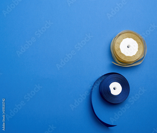 spools with blue and golden satin ribbon on a blue background