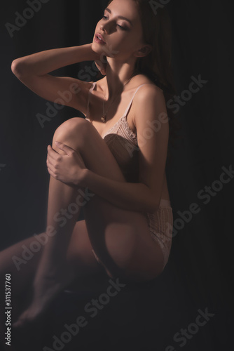 sensual young woman in lingerie posing while sitting on black background © LIGHTFIELD STUDIOS