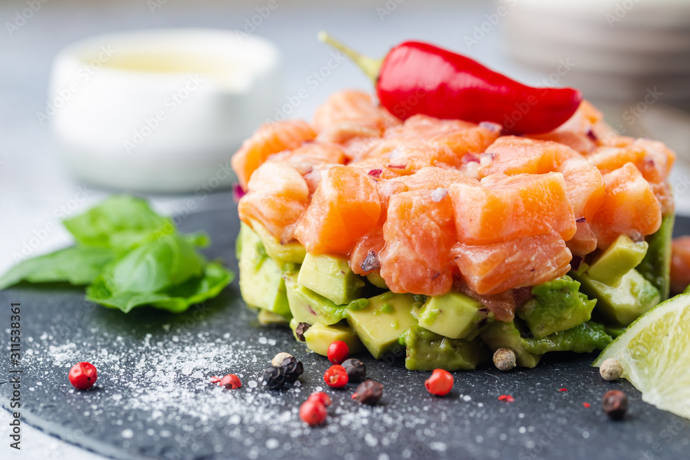 Delicious avocado and raw salmon salad, tartare, served on a black plate with lime, light background - obrazy, fototapety, plakaty 