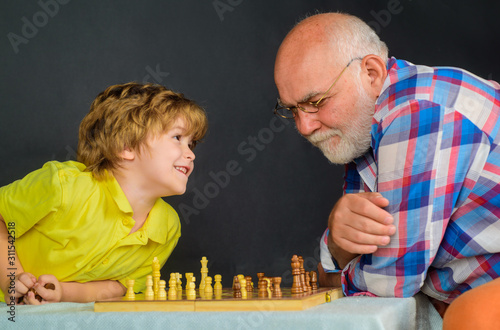 Grandpa and grandson playing chess enjoying leisure time. Chess match. Board games. Handsome grandfather and grandson playing chess spending time together. Little boy playing chess with grandfather.