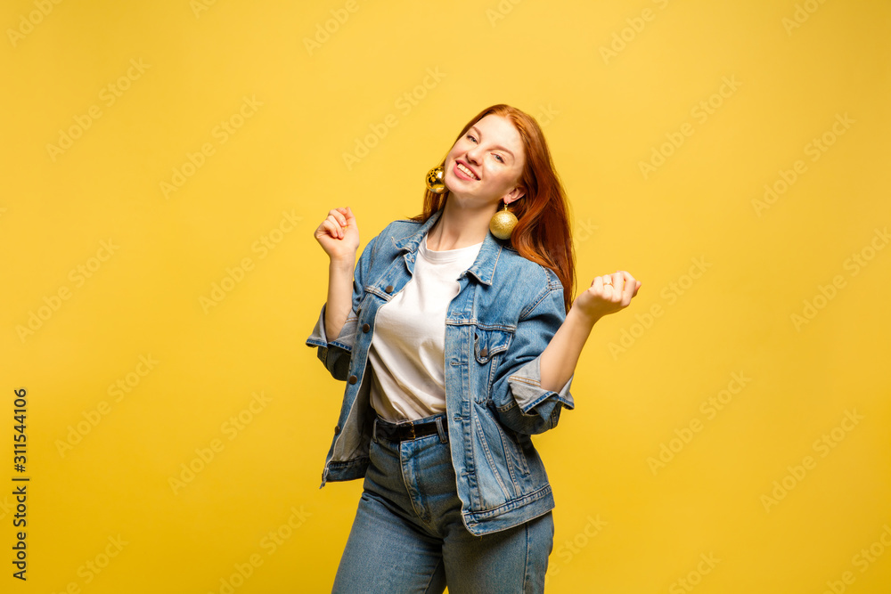 New Year's look. Caucasian woman's portrait on yellow studio background. Beautiful female red hair model in jeanse. Concept of human emotions, facial expression, sales, ad, winter mood, Christmas. New Year's look. Caucasian woman's portrait on yellow studio background. Beautiful female red hair model in jeanse. Concept of human emotions, facial expression, sales, ad, winter mood, Christmas.