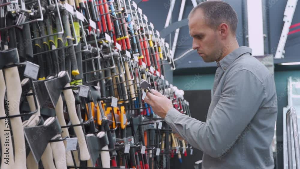 Male buyer holding two hammers in hardware store