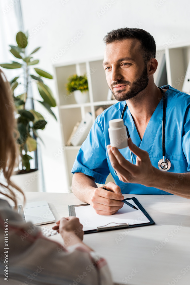 selective focus of handsome doctor holding bottle with pills near woman
