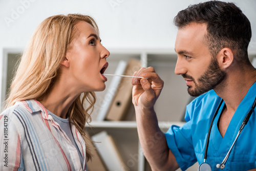 side view of handsome doctor examining woman with medical spatula