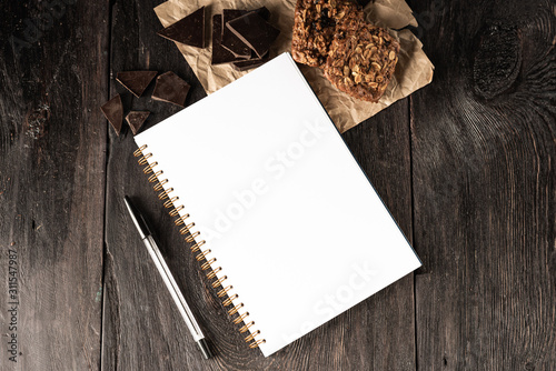Notebook for culinary notes and a pen on the table. muffins and pieces of chocolate on the table. Cook business concept