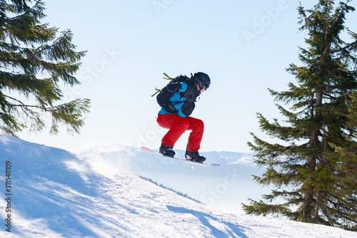 Snowboarder Jumping on the Red Snowboard in Mountains at Sunny Day. Snowboarding and Winter Sports