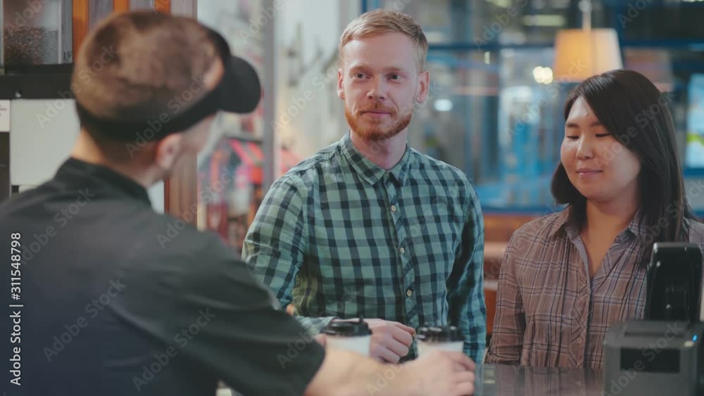 Young diverse couple buy takeaway coffee in fastfood cafe. Asian girl and caucasian ginger bearded hipster take away coffe in paper cups and go away
