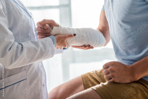 cropped view of orthopedist touching injured arm of man photo