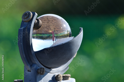 Weather station and the sun in a blue sky reflected in the glass sphere of a beautiful heliograph on a green background photo