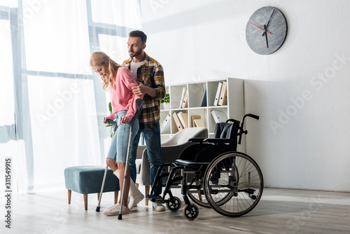 wheelchair near injured woman holding crutches while standing with man photo