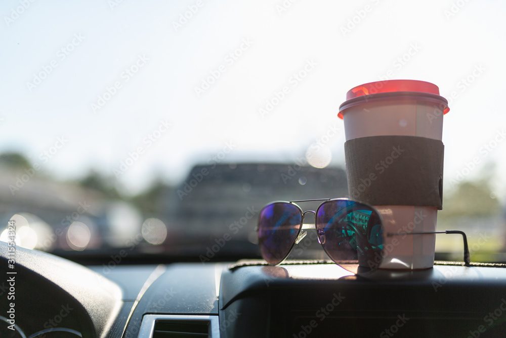 White paper coffee Cup and sunglasses on the dashboard of the car. Paper Cup with hot tea and