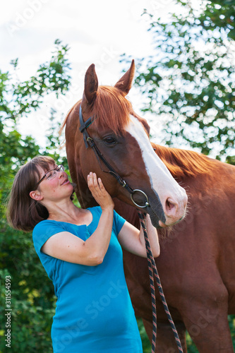 Smiling young pregnant woman talking to her horse