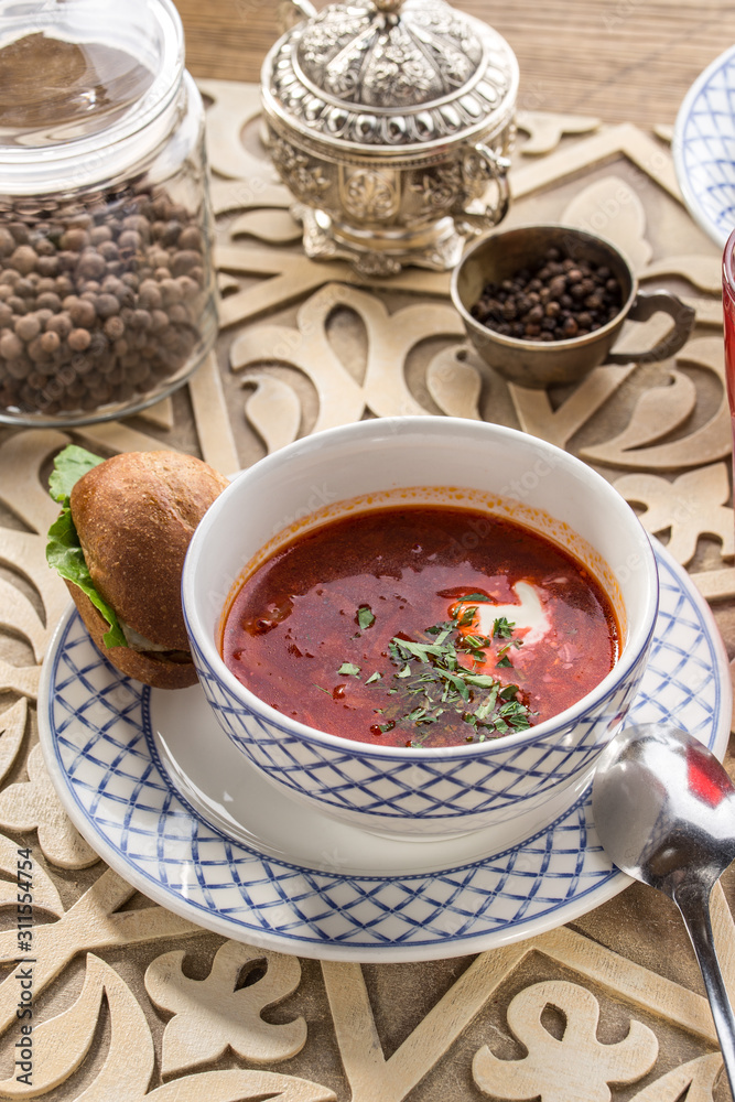 Red beetroot soup borshch with bread bun and sour cream on oriental wooden table Red beetroot soup borshch with bread bun and sour cream on oriental wooden table